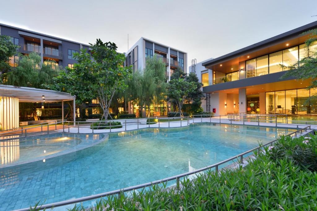 A broad outdoor pool bordered by planting, covered seating, and glass-fronted hotel spaces.