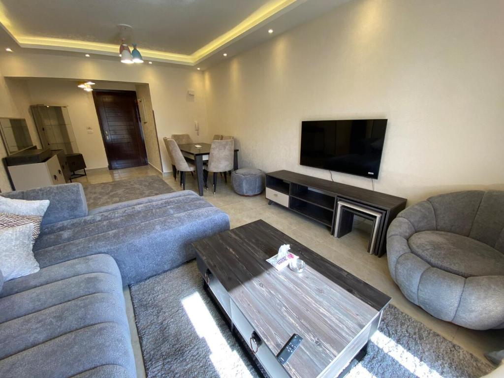 Una sala de estar con un sofá, un televisor y una mesa. en Alrehab Cheapest and awesome, en Burg el-Ḥudûd