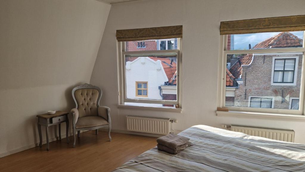 a bedroom with a bed and a chair and two windows at Family rooms in central, historic Gouda in Gouda
