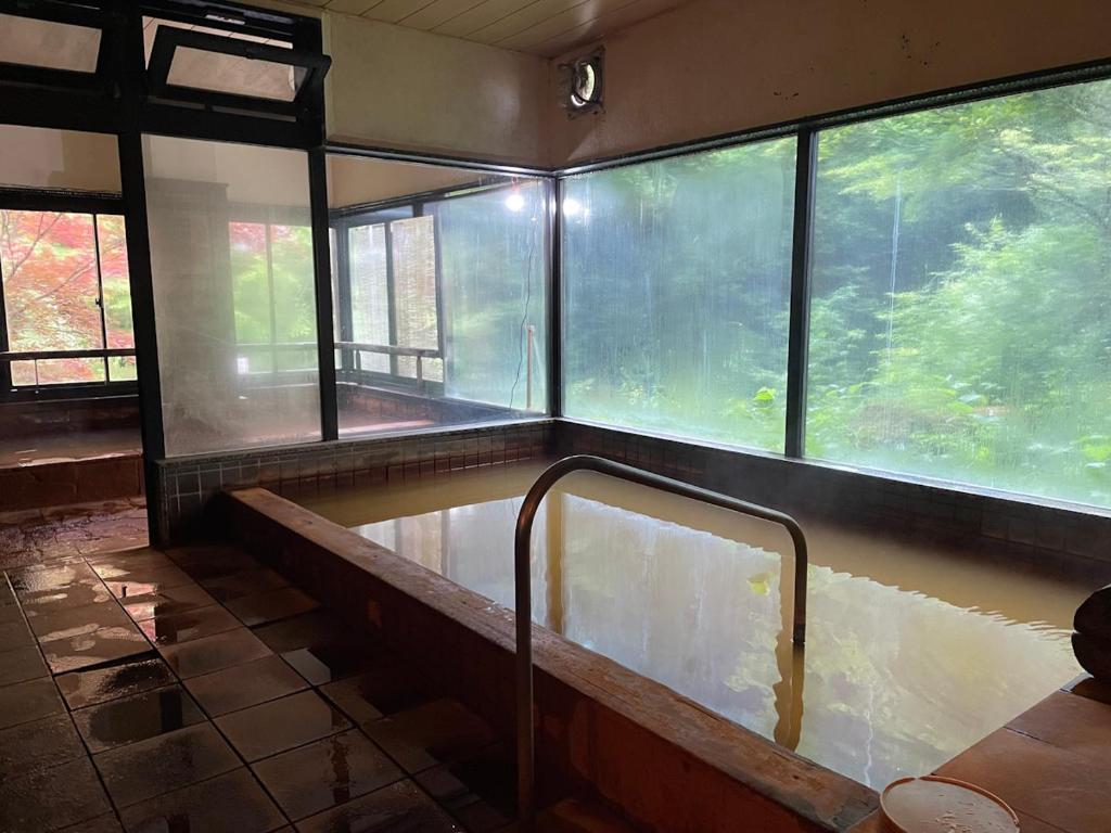 une baignoire dans une pièce avec des fenêtres dans l'établissement Yama no Yado Meiji Onsen, à Chino