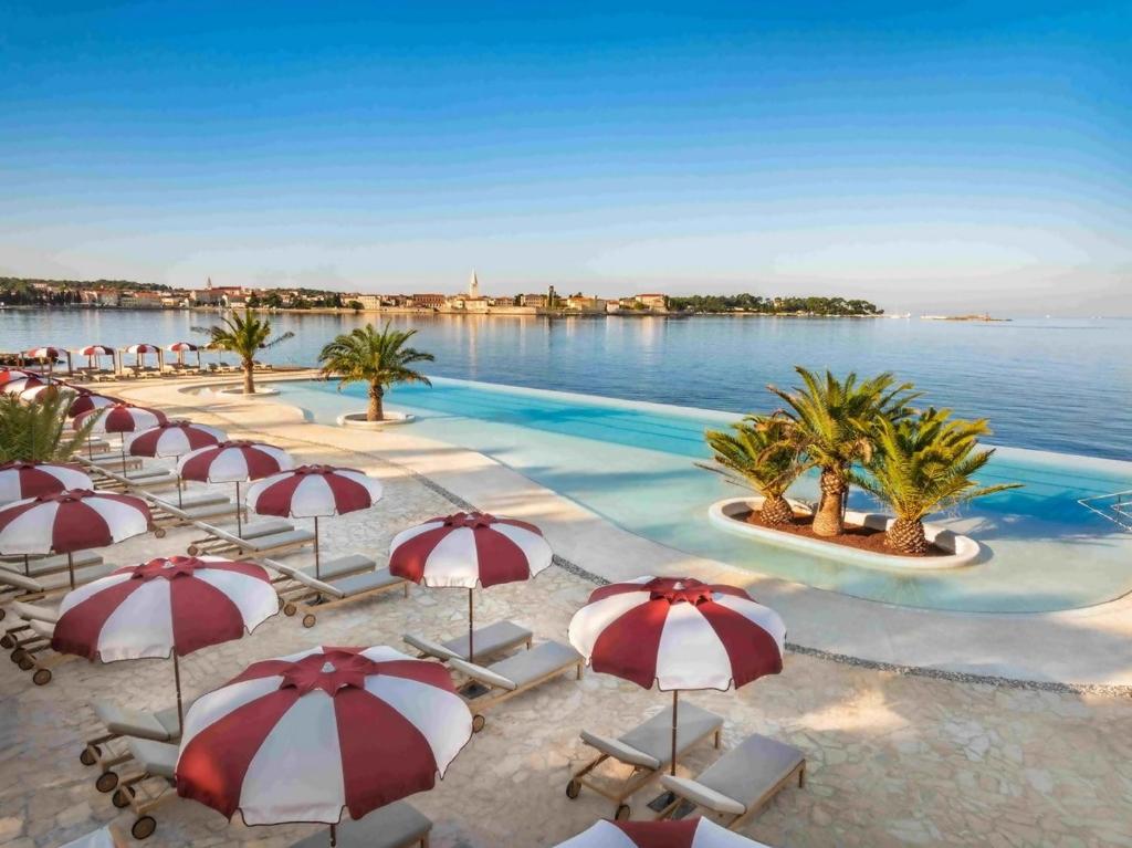 a pool with red and white umbrellas and the water at New!!! NEW RIVA LUXURY ONE - with sunny terrace & big garden in Poreč