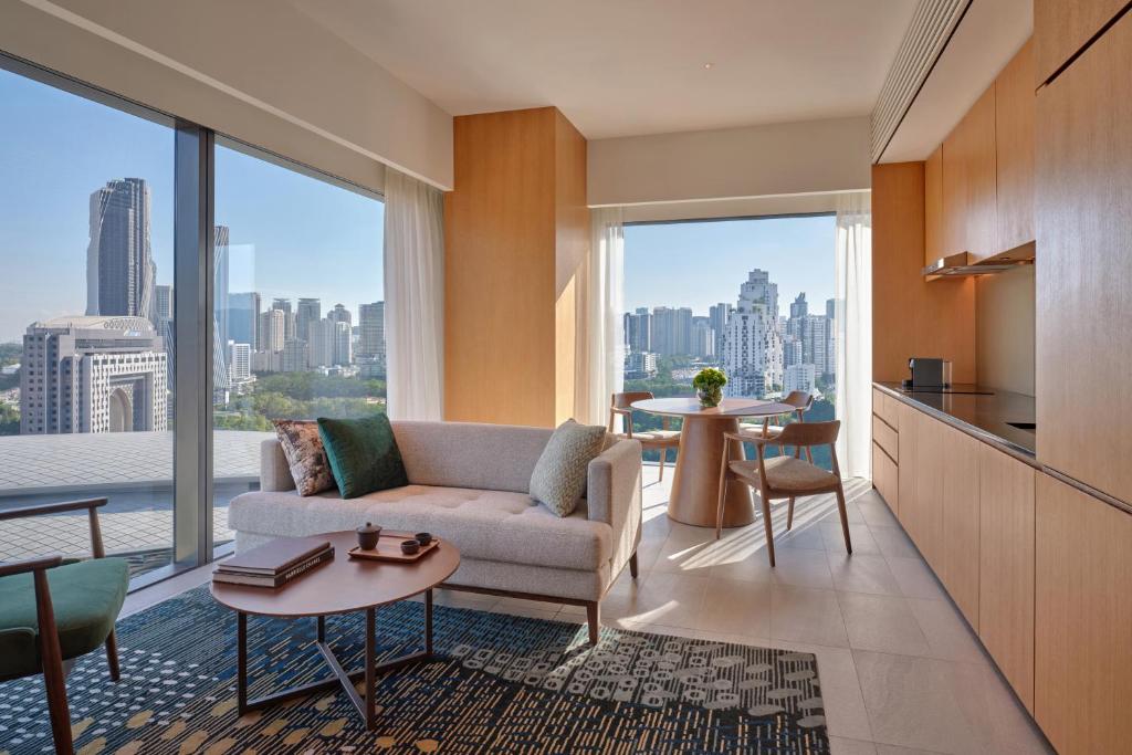 A sunlit sitting room with a sofa, dining table and broad city views.