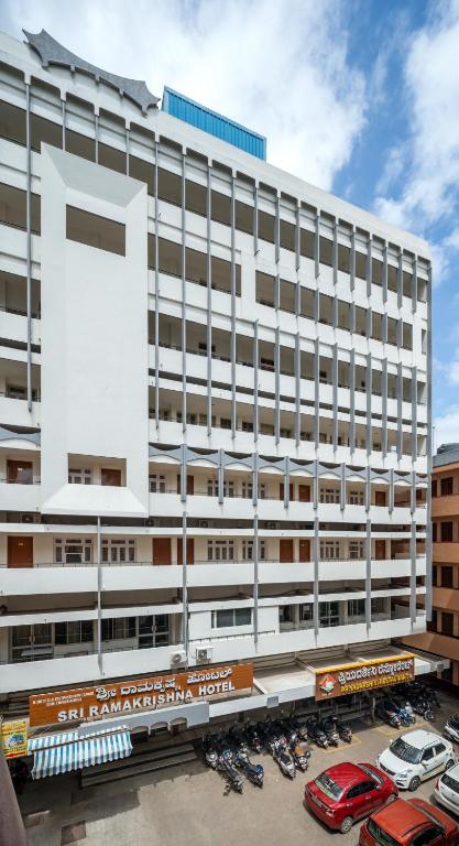 a large white building with cars parked in a parking lot at Sri Ramakrishna Hotel in Bangalore