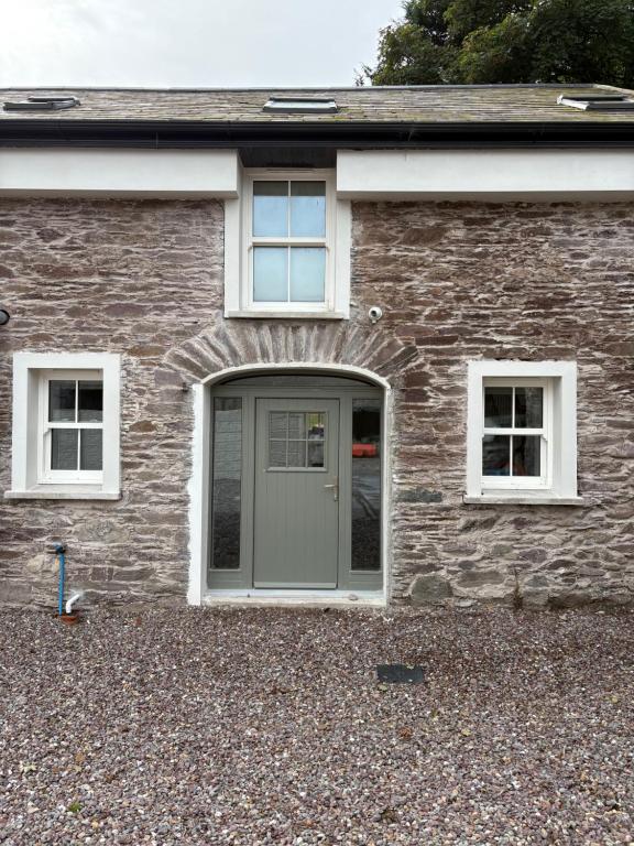 a brick house with a gray door and two windows at The Courtyard Apartments in Macroom