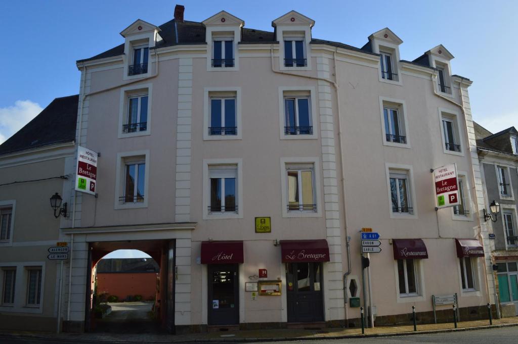 a large white building with an archway on a street at Logis Le Bretagne in Sillé-le-Guillaume