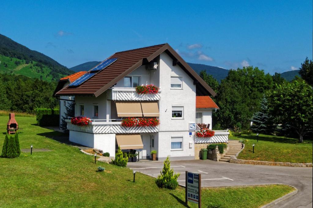 una casa blanca con flores rojas en las ventanas en Guesthouse Franjkovic, en Selište Drežničko