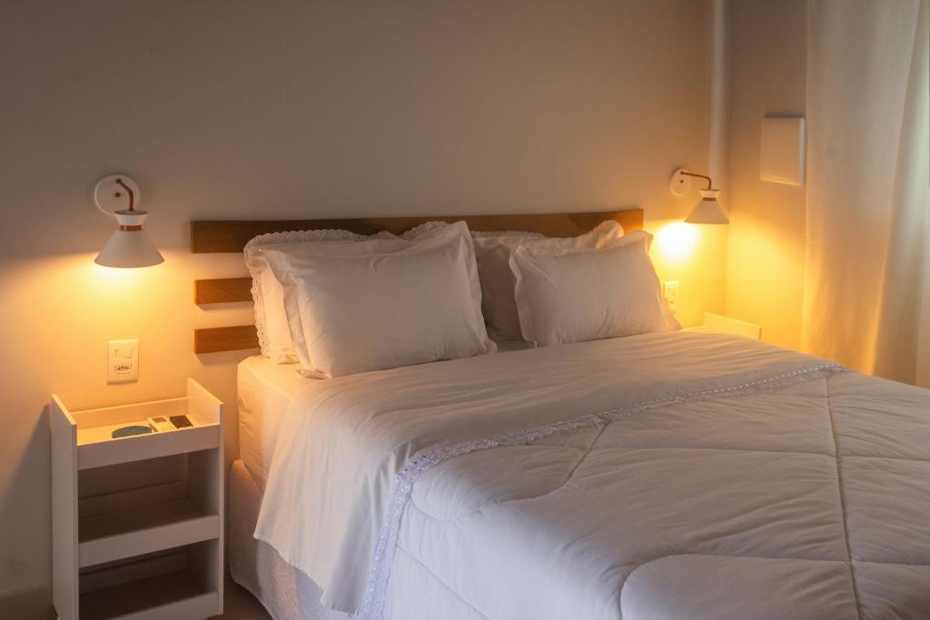 a bedroom with a white bed with two lamps at Pousada Aromas do Vale in Chapada dos Guimarães