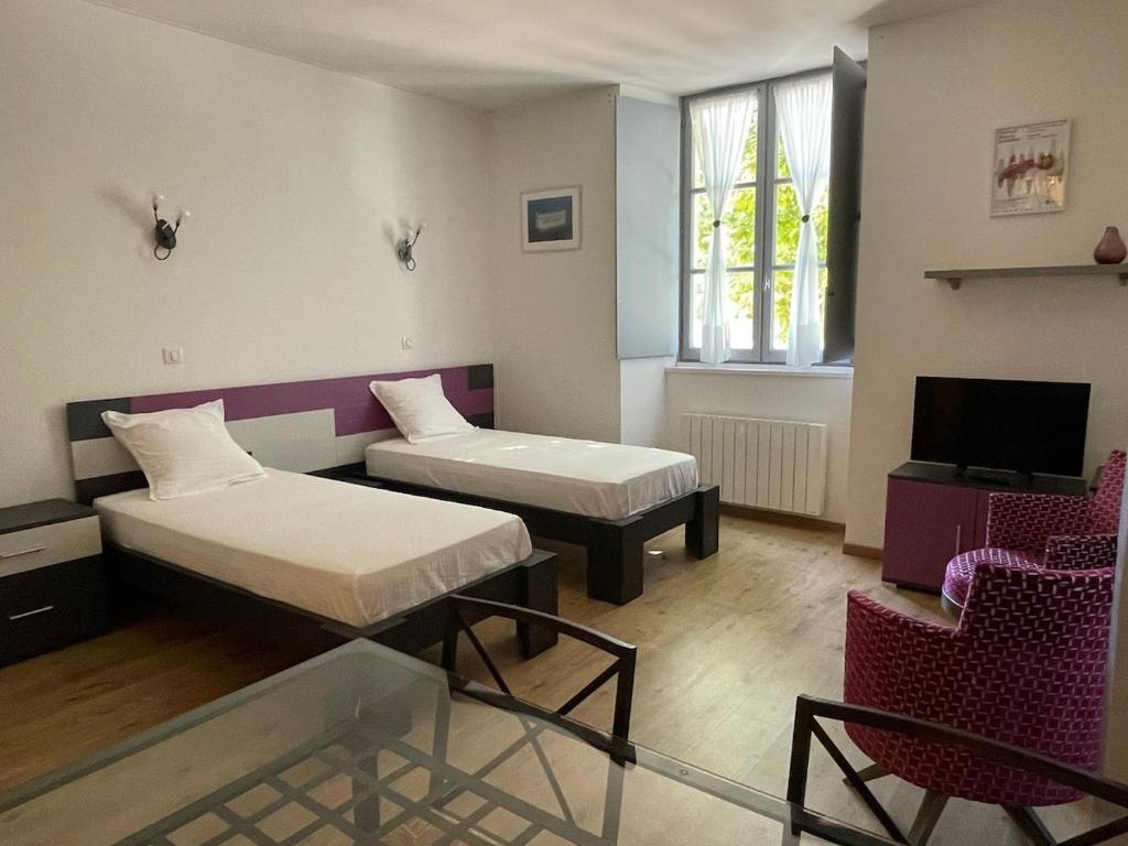 a room with two beds and a tv and a chair at Le Studio des Demoiselles in Rochefort