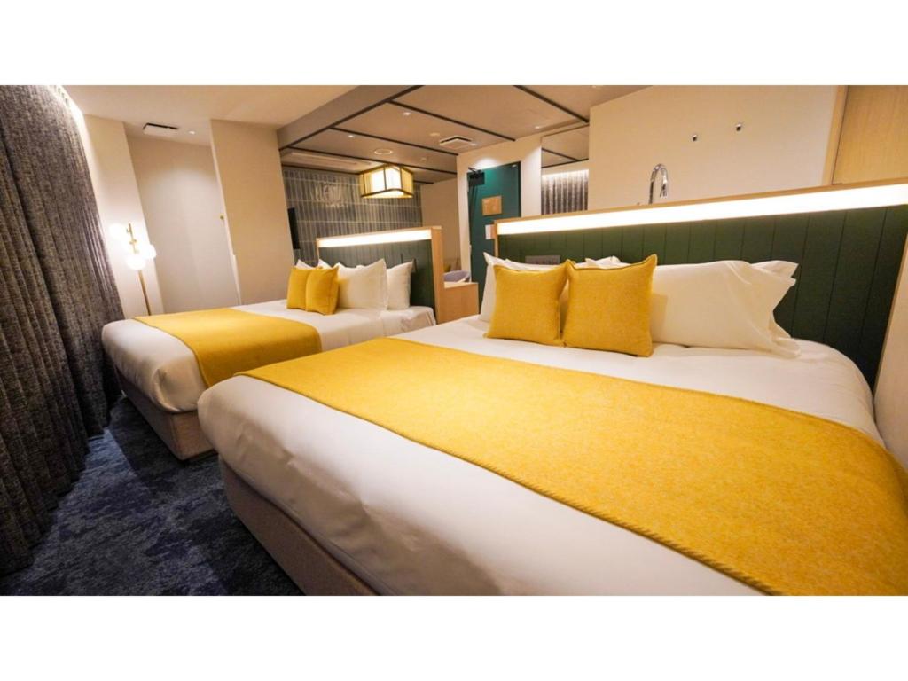 two beds in a hotel room with yellow pillows at THE GALA HOTEL UMEDA - Vacation STAY 24233v in Osaka
