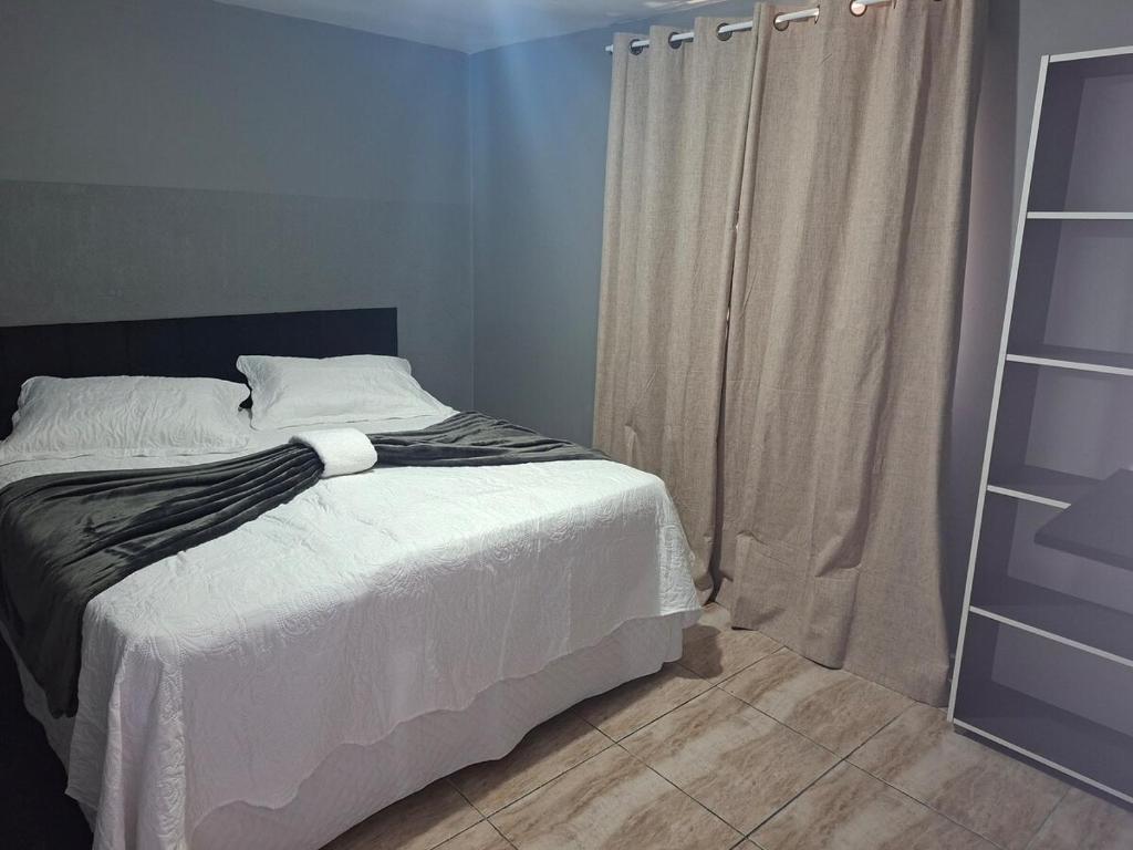 a bedroom with a bed with white sheets and a window at Apartamento para família in Guarapuava