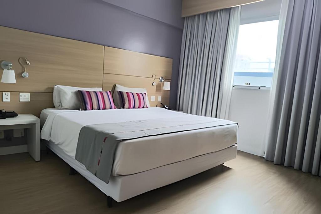 um quarto com uma grande cama branca com almofadas cor-de-rosa em Suíte em flat no Gonzaga Stay Helbor em Santos