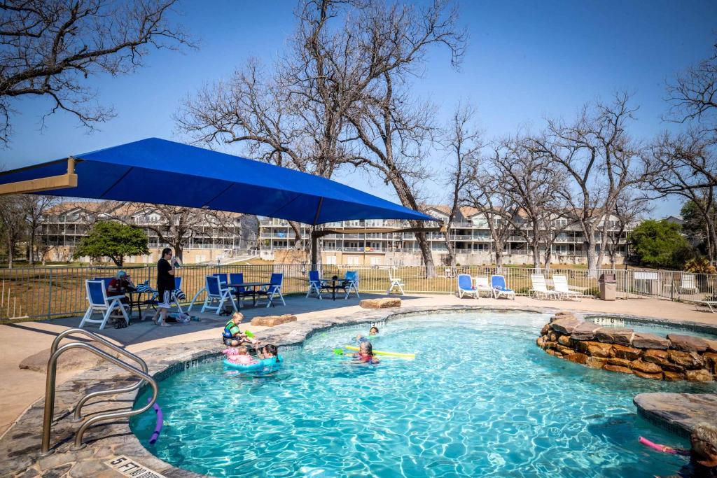 a group of people in a swimming pool with a blue umbrella at Shared Heated Pool Balcony BBQ Near Downtown in New Braunfels