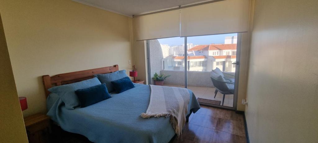 a bedroom with a bed with blue pillows and a balcony at Avenida del Mar Condominio Oceanic in La Serena