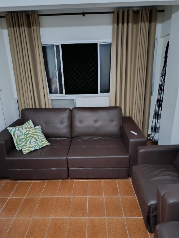 eine braune Ledercouch in einem Wohnzimmer mit Fenster in der Unterkunft Caiçara de frente para mar in Praia Grande