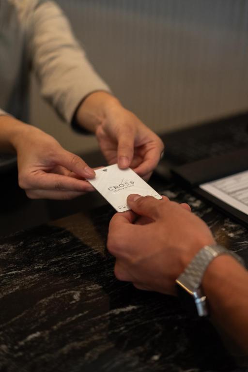 Hands exchange a small card across a dark reception counter beside a laptop.