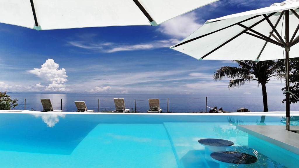 圣胡安Kawayan Holiday Resort的一个带遮阳伞和椅子的游泳池以及大海