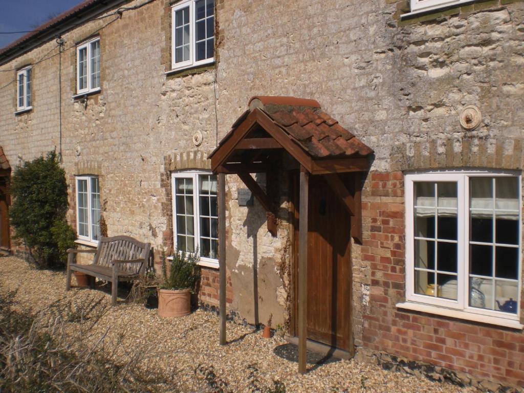 a brick building with a wooden door and a bench at Bluebell and Appletree Cottages in Hockwold cum Wilton