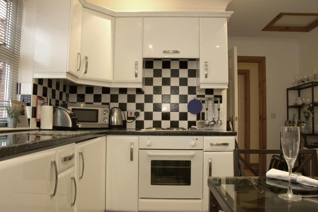 a kitchen with white cabinets and a black and white checkered wall at Pintail Apartment Bamburgh in Bamburgh