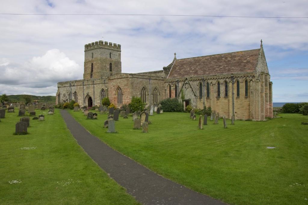 an old church with a cemetery in the grass at Pintail Apartment Bamburgh in Bamburgh