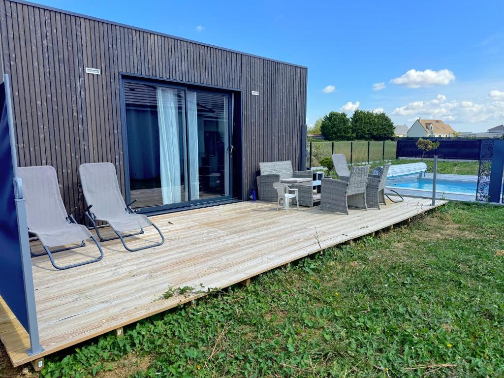 een houten terras met stoelen en een tafel en een zwembad bij Tiny house - piscine et vélos in Vasselay