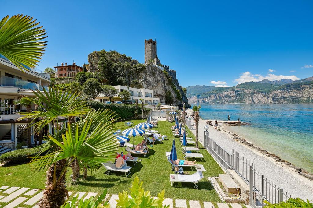 een strand met stoelen en parasols naast het water bij Hotel Castello Lake Front in Malcesine
