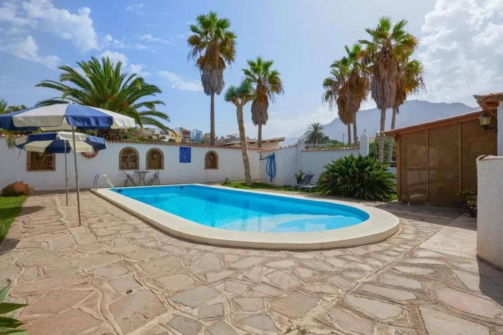 a swimming pool in front of a house with palm trees at Charming House with Pool in Buenavista del Norte in Buenavista del Norte