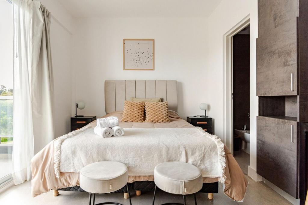 a bedroom with a large bed with two stools at Retrato Urbano Ezeiza G&A Rent in Ezeiza