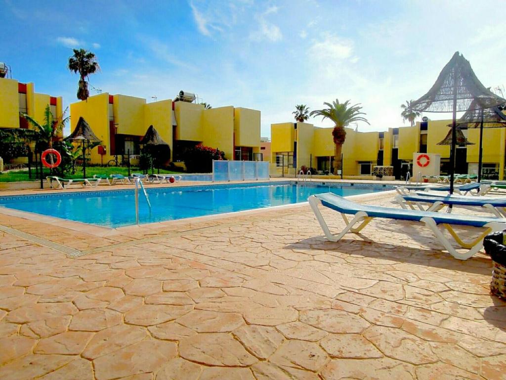 a swimming pool with two chairs in front of a building at Duplex El Cortijo, LasAmericas in Playa de las Americas