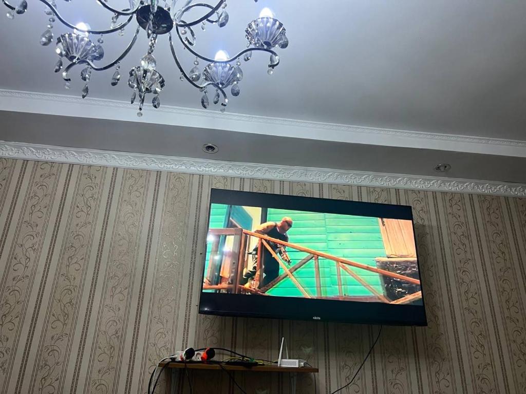 a flat screen tv hanging on a wall with a chandelier at Family Stay Karakol in Karakol
