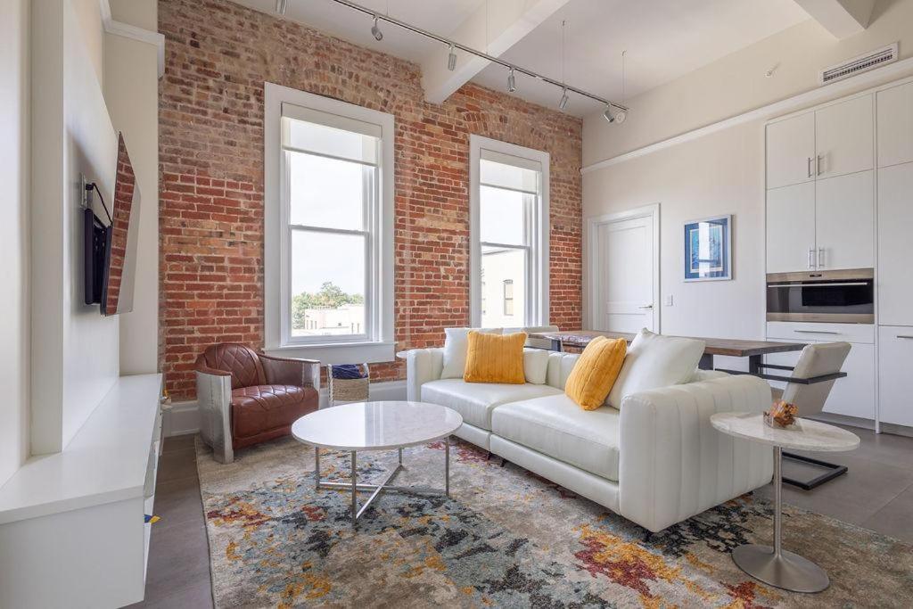 a living room with a white couch and a brick wall at Lofty Blues at the Brent Lofts in Baptist Hospital Heliport