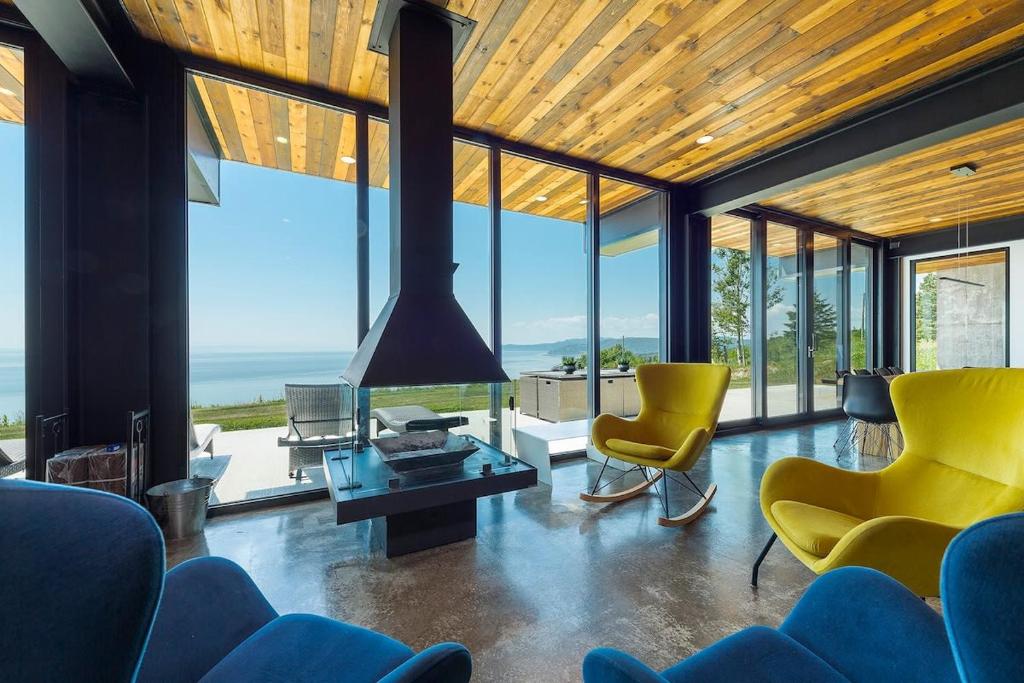 een woonkamer met gele stoelen en ramen bij Chalet L'Eaurizon Charlevoix in La Malbaie