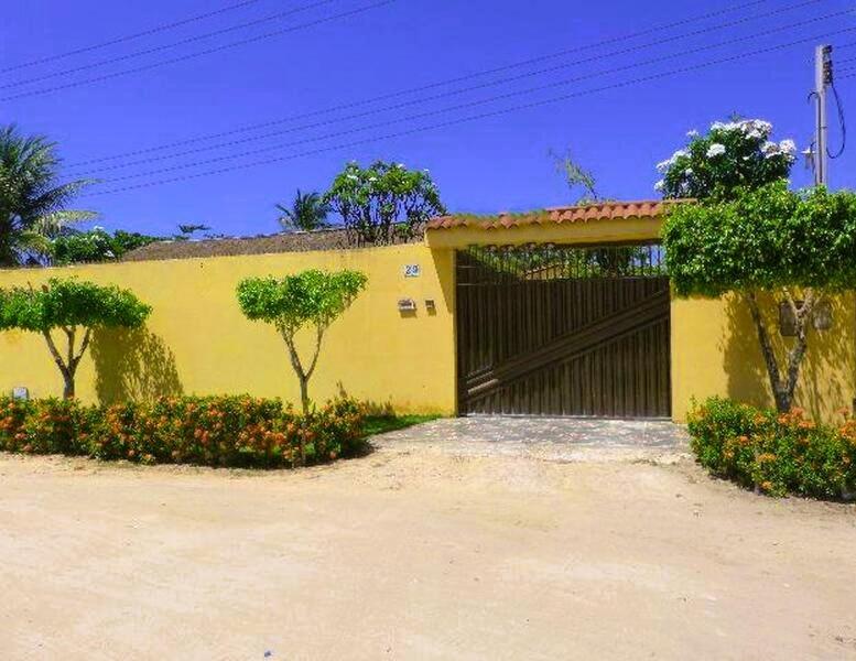 a yellow garage with a black gate and some trees at Cantinho da paz in Maragogi