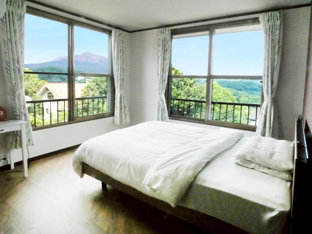 a bedroom with a large bed and large windows at Onsen Villa Kuon Kirishima in Kirishima