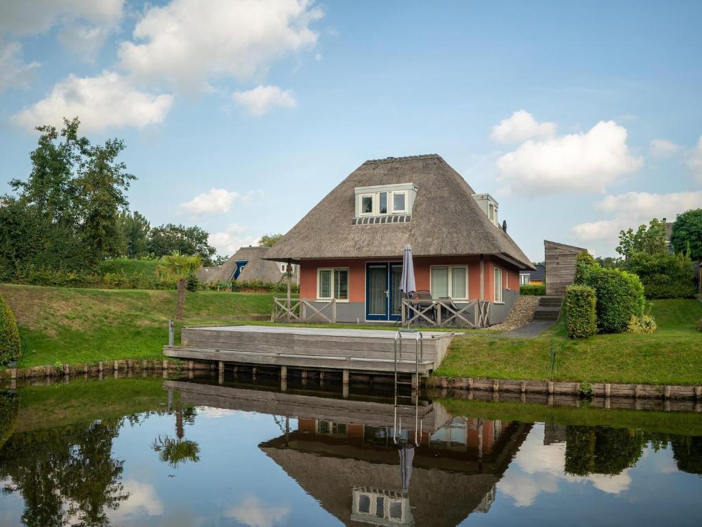a house with a thatched roof reflecting in the water at Comfortable Waterfront Park Retreat in Midlaren
