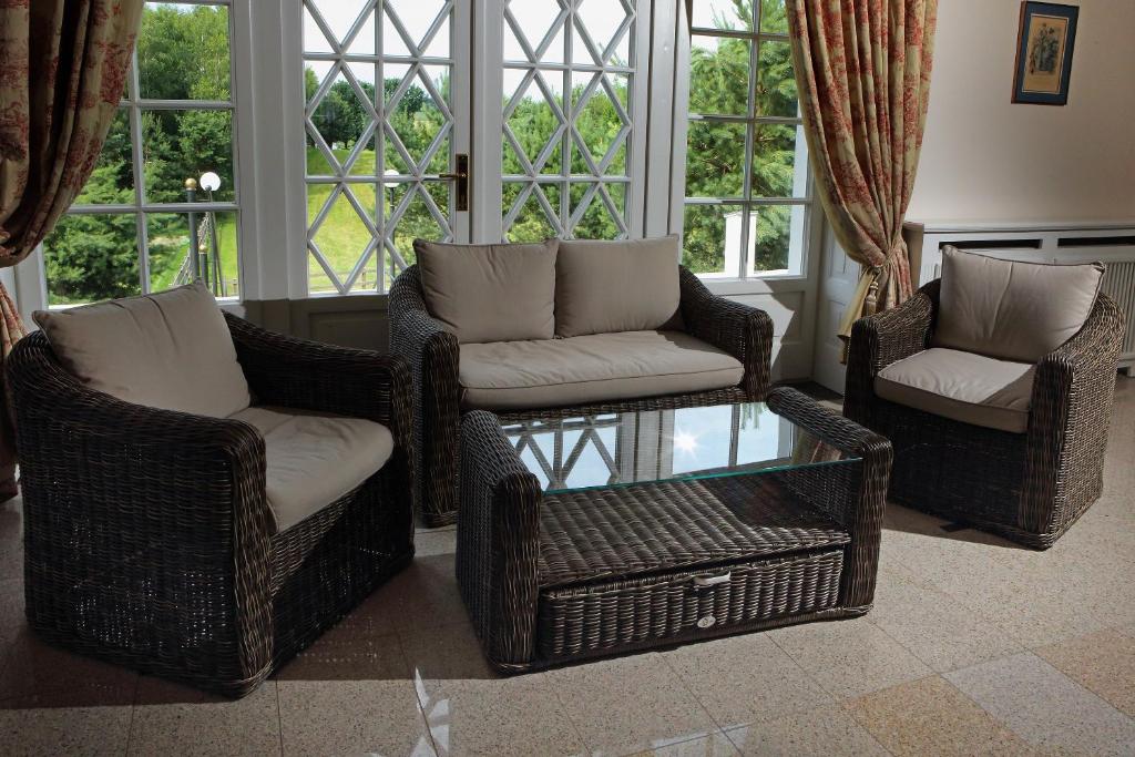 Wicker seating set with glass coffee table in bright sunroom, large diamond-pane windows and patterned curtains.