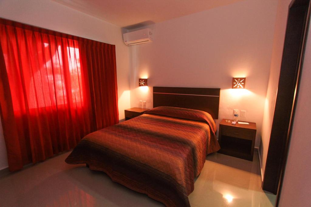 カンクンにあるホテル ロス ヒラソレスのベッドと赤いカーテンが備わるホテルルームです。