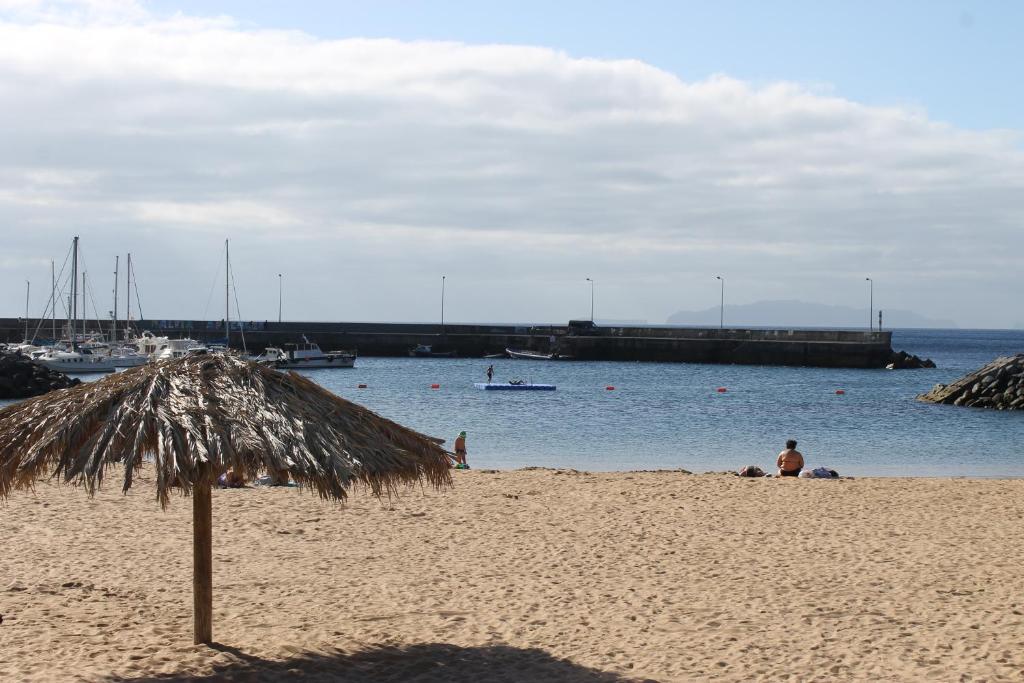 un ombrellone di paglia su una spiaggia con acqua di Cozy and Bright Apartment a Machico