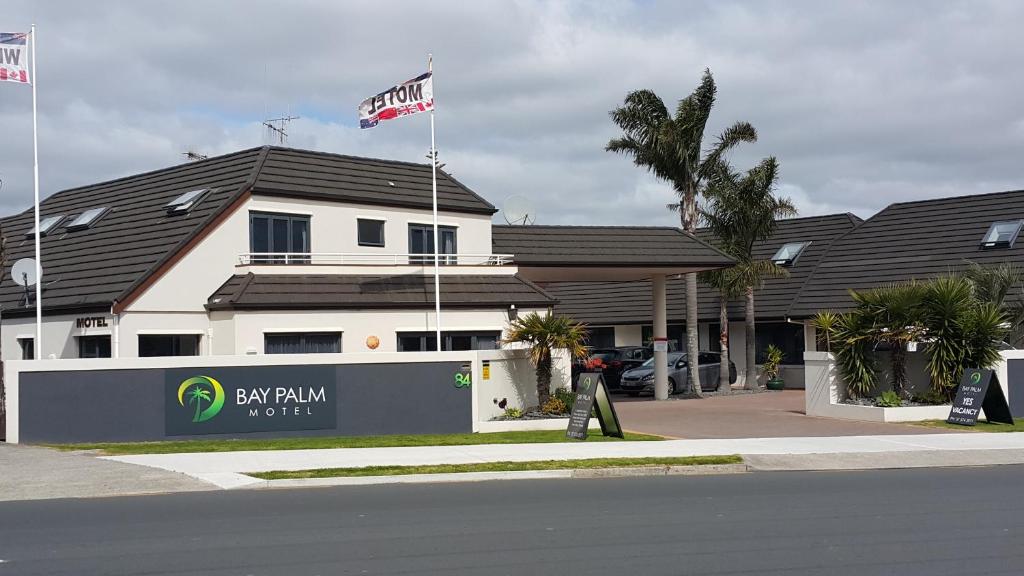 Un uomo in piedi di fronte a un edificio con due bandiere di Bay Palm Motel a Mount Maunganui