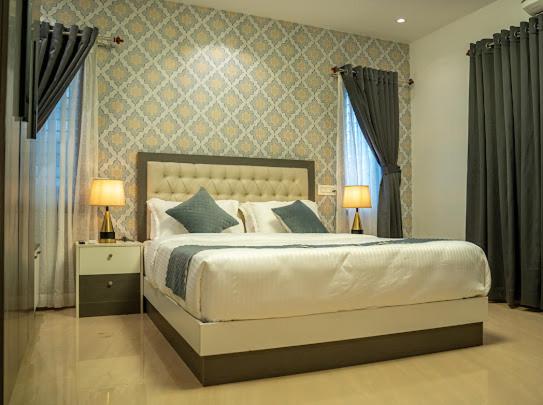 a bedroom with a bed with two lamps and two windows at FA Gardens in Ernakulam