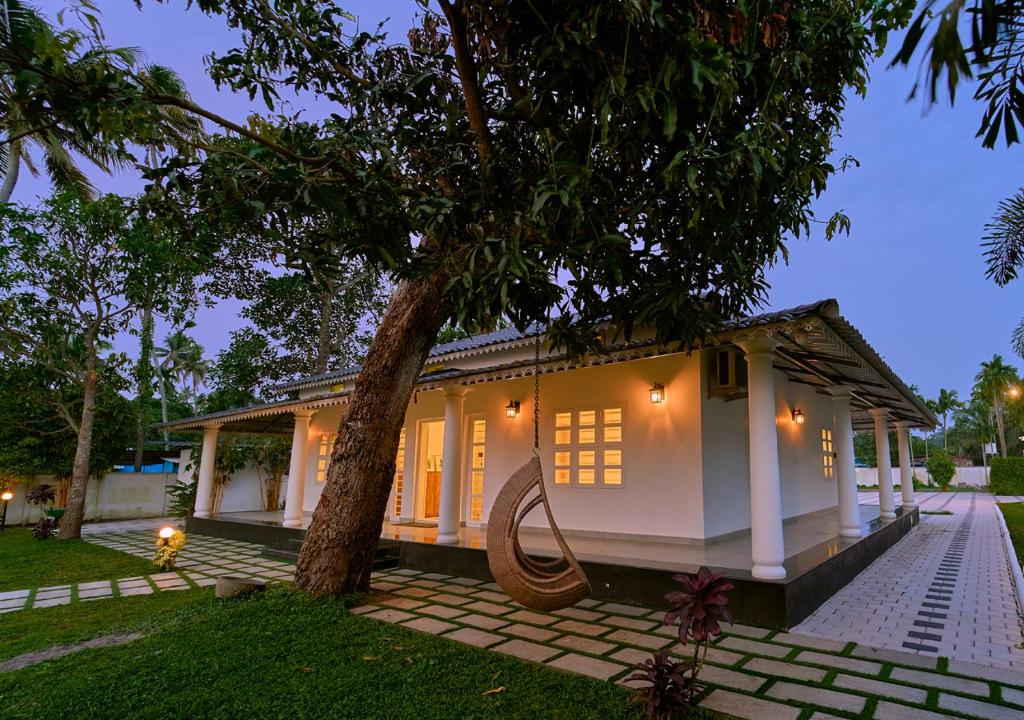 a small white house with a tree in the yard at Ashtamudi Lake Villa by VOYE HOMES - Pet Friendly & Events Welcome in Kollam