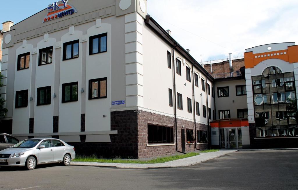 ein weißes Gebäude mit einem davor geparkt in der Unterkunft Hotel SKY CENTR Krasnoyarsk in Krasnojarsk