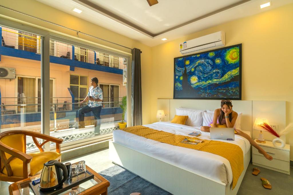 a woman sitting on a bed with a laptop in a bedroom at The Social Stays Rishikesh in Rishīkesh