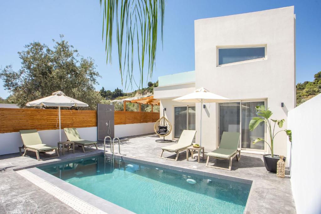 a swimming pool with chairs and umbrellas next to a house at Aura Luxury Villas in Kolymbia