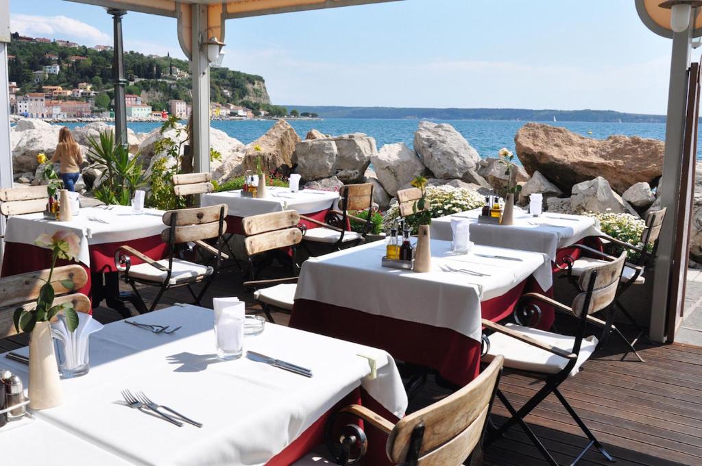 un restaurant avec des tables et des chaises blanches et l'océan dans l'établissement Apartments & Rooms Riva, à Piran