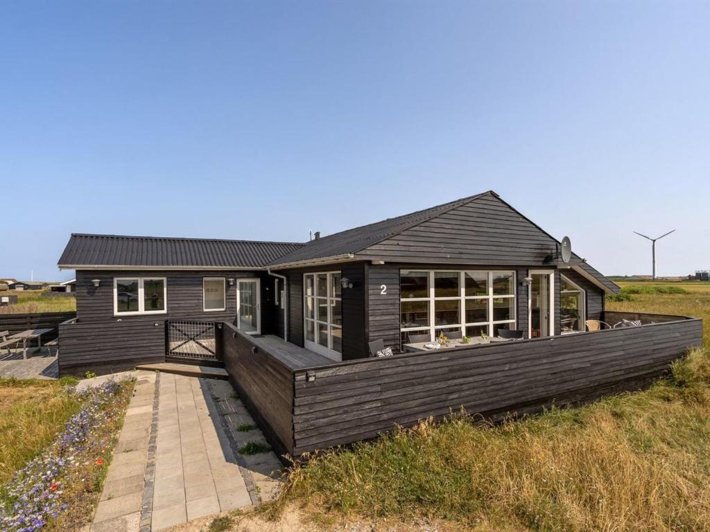 a black house with a deck in a field at Holiday Home Withger - 300m from the sea by Interhome in Harboør