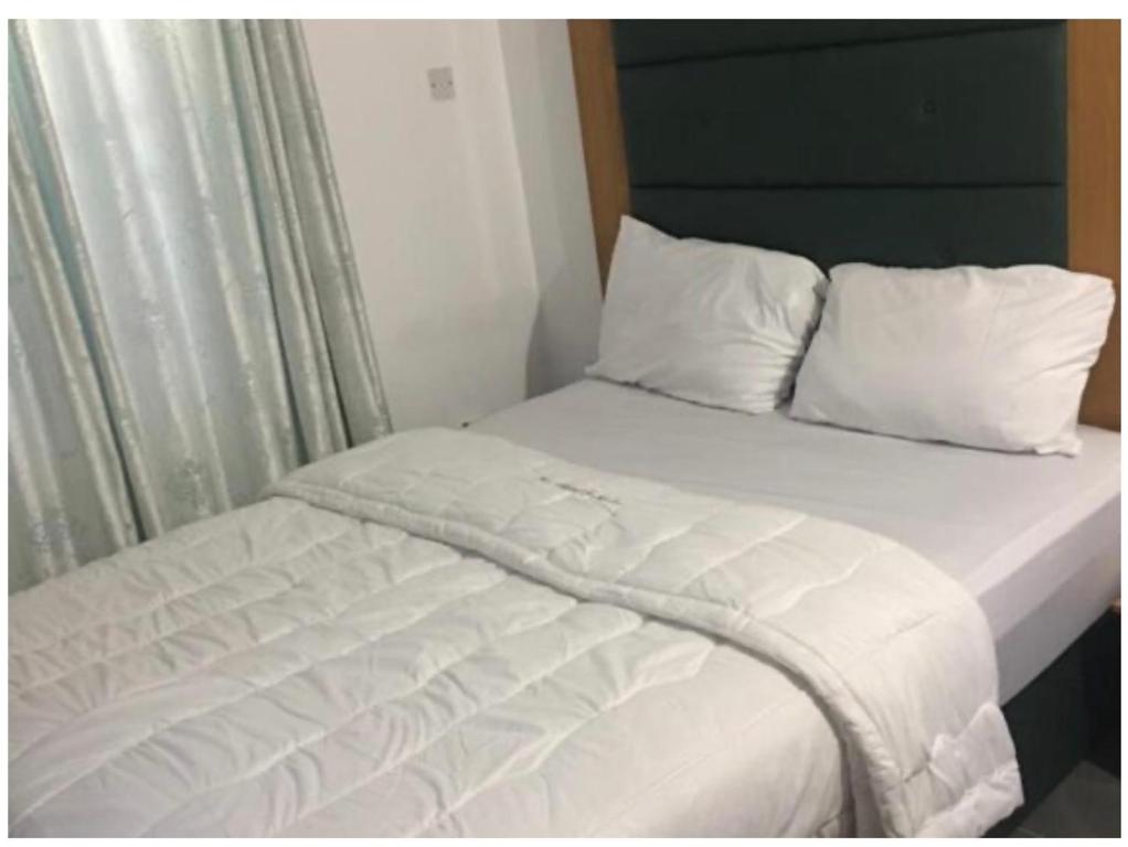 Cama con sábanas blancas y almohadas junto a una ventana en Epe Hotels & Suites, en Epe