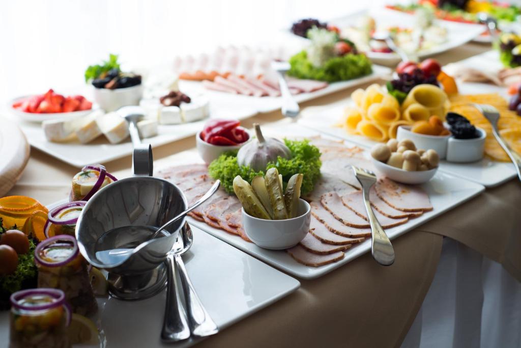 Buffet spread with sliced cold meats, pickles, condiments and serving utensils on white platters