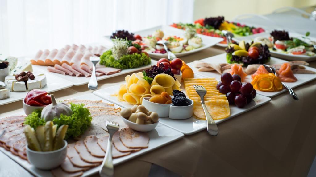Breakfast buffet spread with assorted cheeses, cold cuts, fruits and garnishes on white platters.