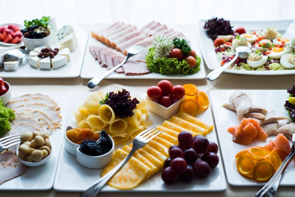 Plates of assorted breakfast buffet items: cheeses, sliced meats, fruits and garnishes.