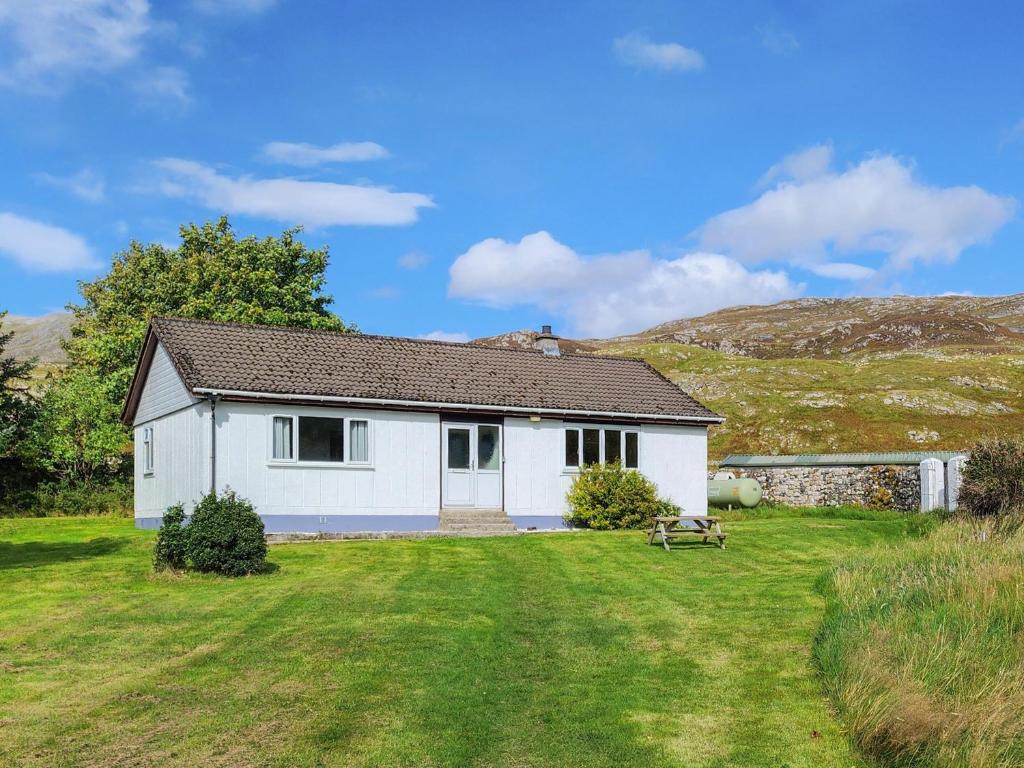 a white house in a field with a grass yard at Walled Cottage - Uk49097 in Inchnadamph